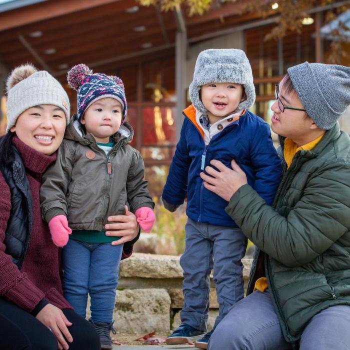 All of Us Hmong family of mom, dad and two young sons outdoors in winter clothing enjoying a late fall day