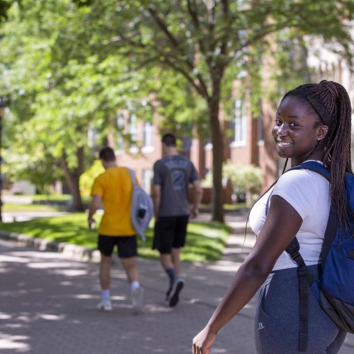 Student walking on campus, looking over her right shoulder and smiling